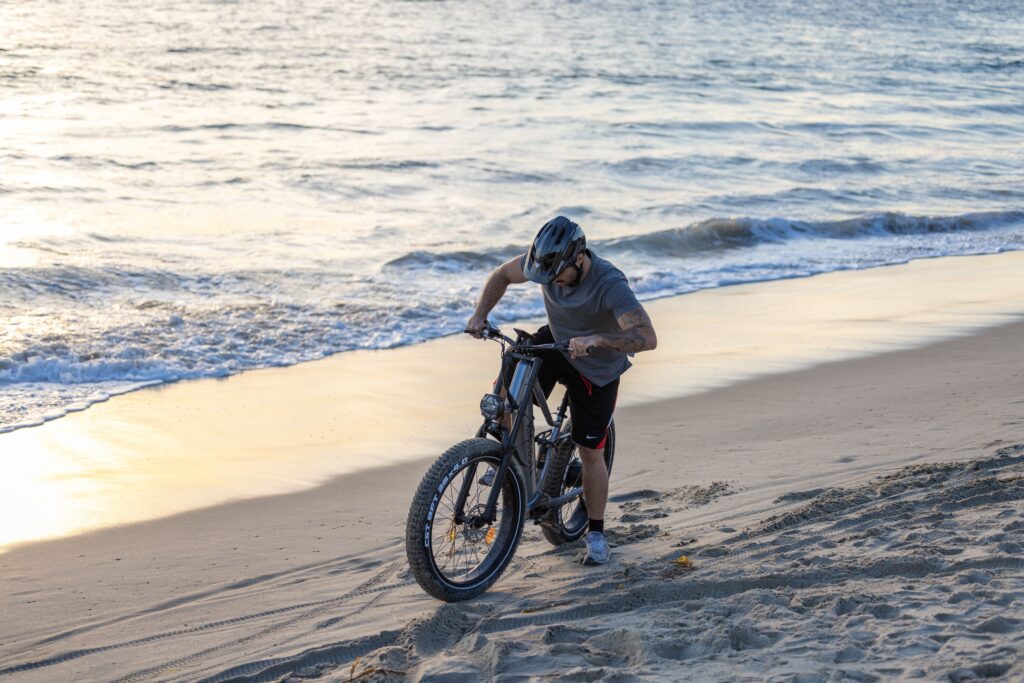 A cyclist pushes his bike along a sandy beach during sunset, blending adventure with tranquility.