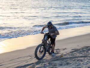 A cyclist pushes his bike along a sandy beach during sunset, blending adventure with tranquility.